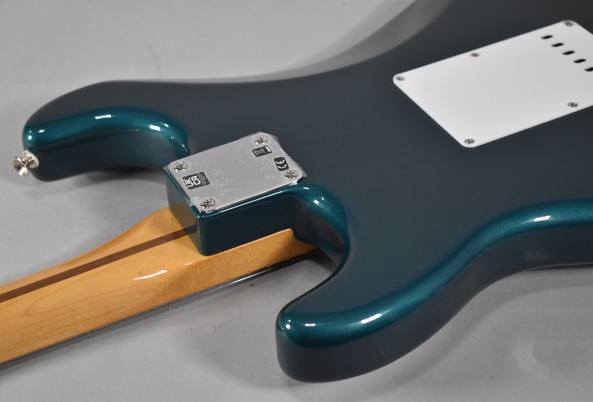 Upper back of a metallic ocean turquoise Stratocaster, showing the neck plate, neck heel, and white tremolo cover.