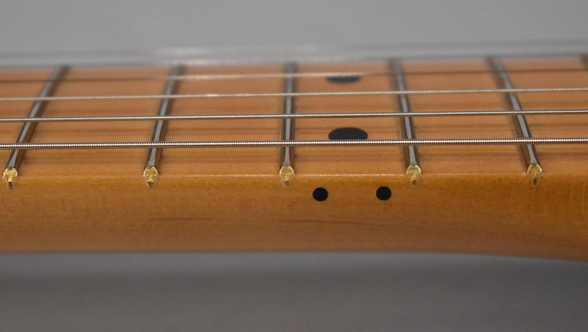 Close-up of the light brown maple neck and fretboard, showing frets 1-5, black dot inlays, and side dots.