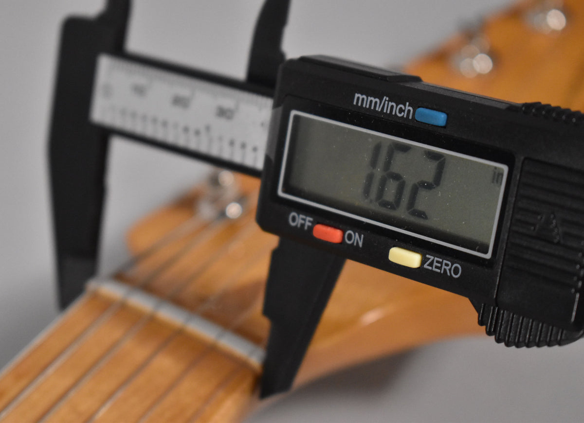 A digital caliper measures the guitar's nut width at 1.62 inches, with the light-colored maple neck and strings visible.