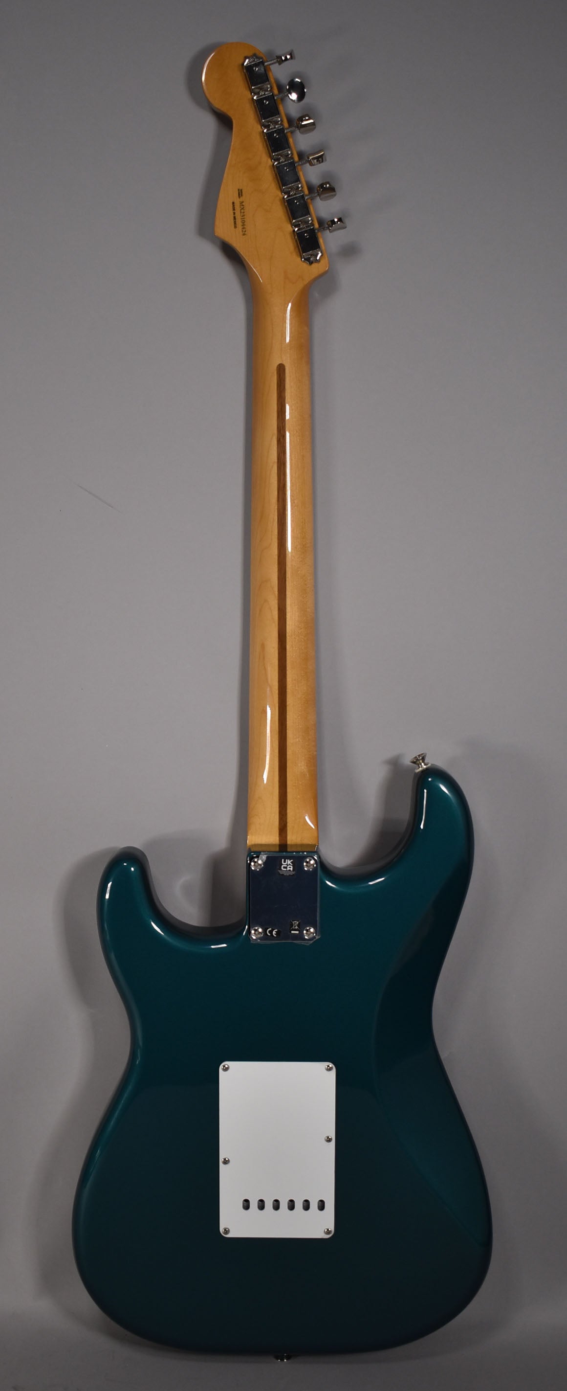The guitar's back, showing a glossy ocean turquoise body, a light maple neck, and a white tremolo cover with six string holes.