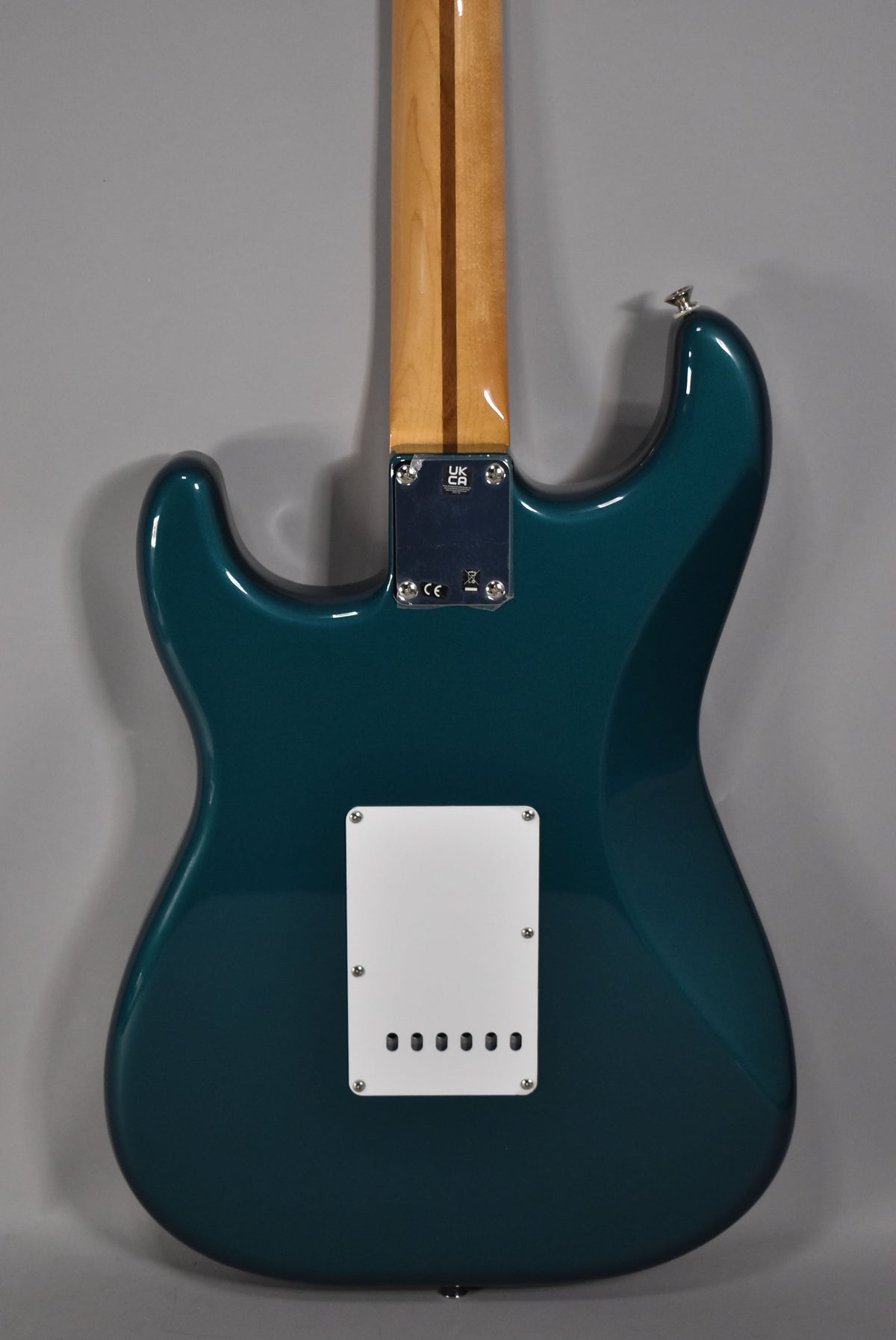 The back of a glossy ocean turquoise electric guitar with a light wood neck and a white rectangular tremolo cover.