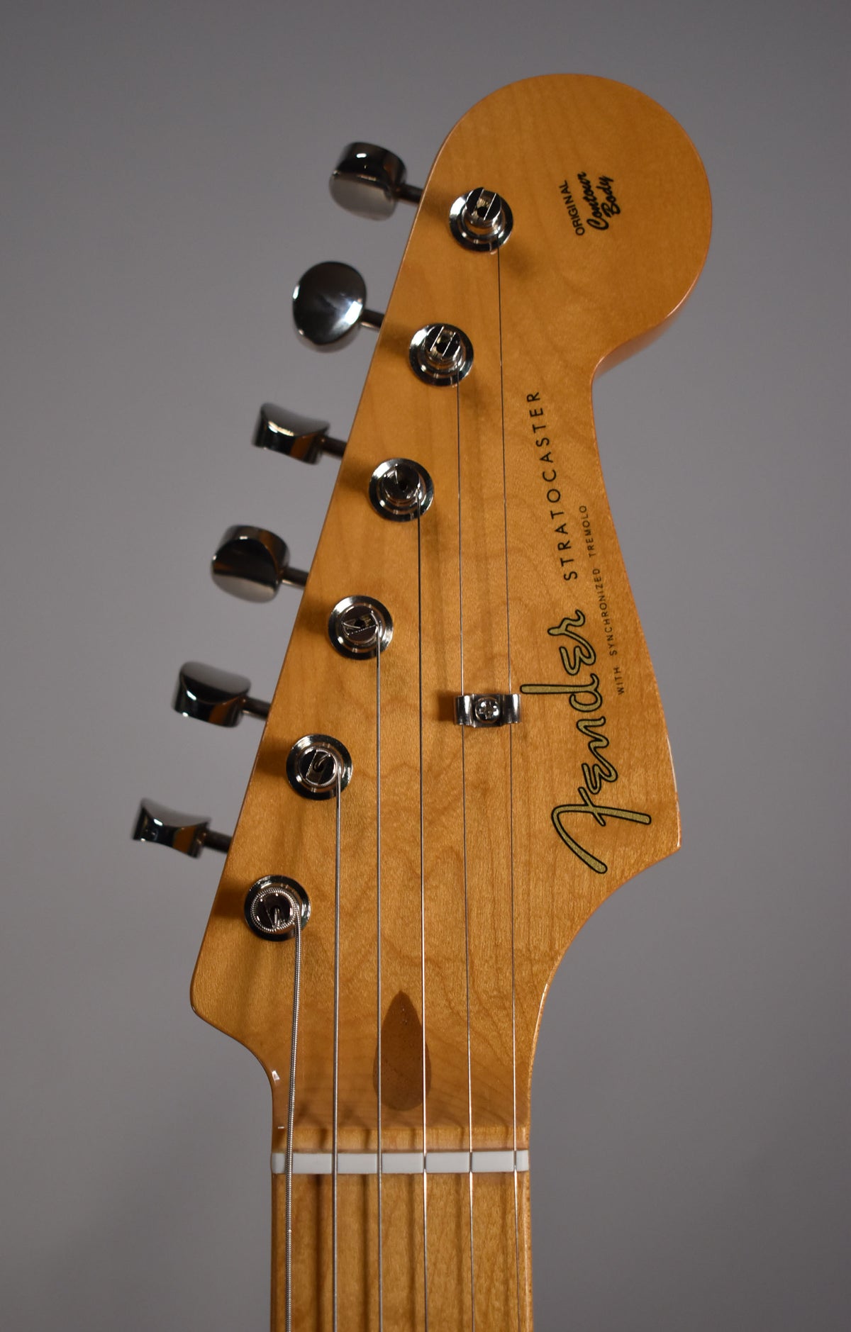 Close-up of a light brown maple headstock with six chrome tuners and a string tree, angled slightly left.