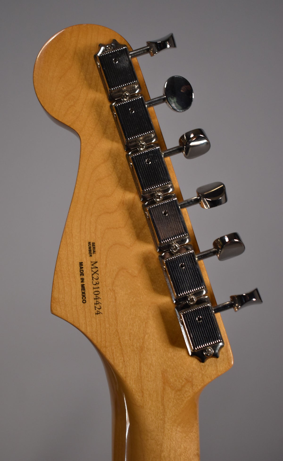 The back of a light wood headstock with a glossy finish, showing six chrome tuning machines with rectangular housings.