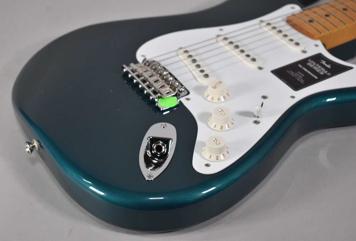 Close-up of the guitar's lower body, showing the metallic ocean turquoise finish, white pickguard, three cream knobs, and output jack.