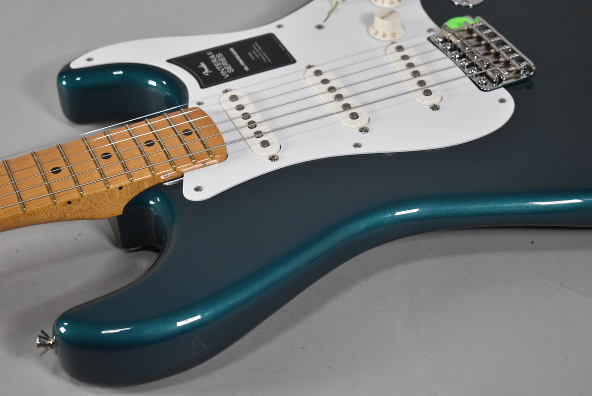 The upper body of an ocean turquoise Stratocaster, showing the maple neck, white pickguard, three single-coil pickups, and chrome bridge.