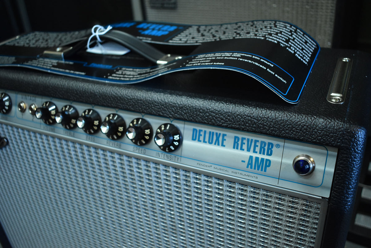 The black textured combo amp is angled, showing its silver control panel with black knobs and a blue pilot light, and a silver grille.