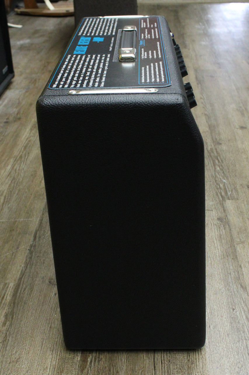 Black combo amp, viewed from the top right, showing the textured Tolex finish, chrome handle, and control panel with black knobs.