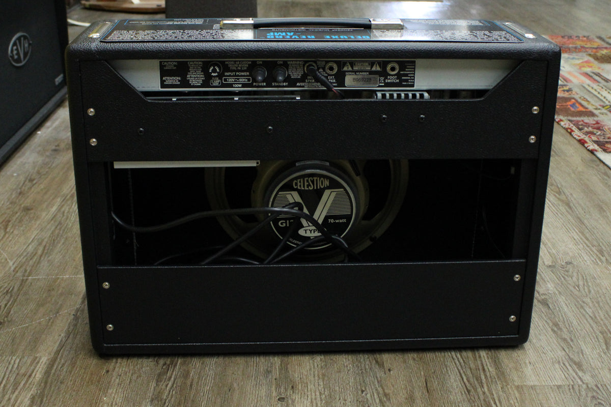 Rear view of a black combo amp, showing the control panel, exposed Celestion G12 speaker, and power cable.