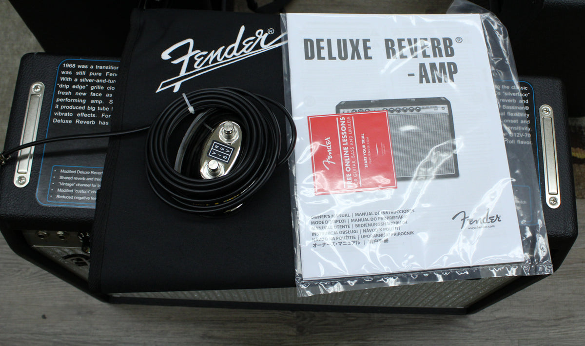 Overhead view of the amp's accessories: a black dust cover, coiled footswitch, and sealed owner's manual.