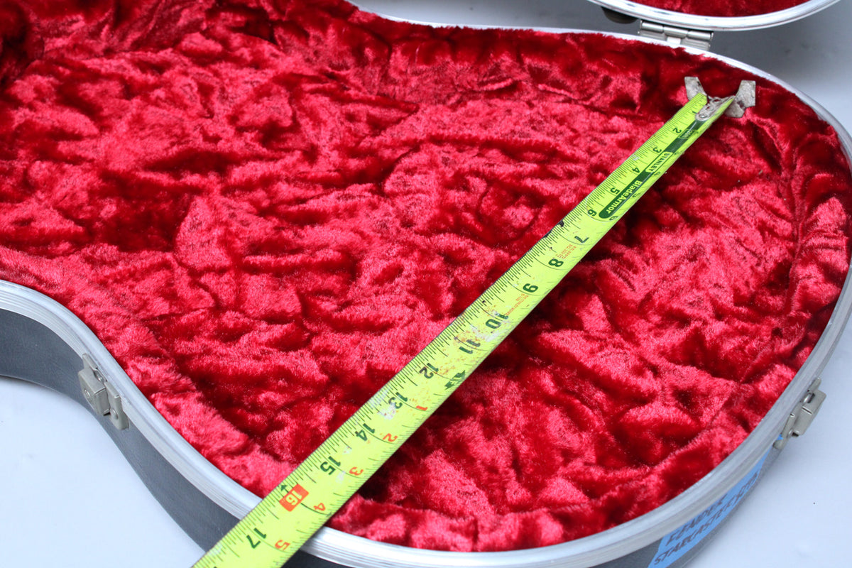 The open black case, lined with plush red crushed velvet, has a yellow tape measure laid diagonally across it.