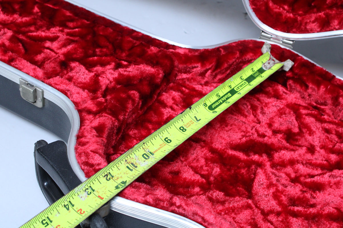 An open black hard case with red plush interior, measured by a yellow tape measure showing 1 to 15 inches.