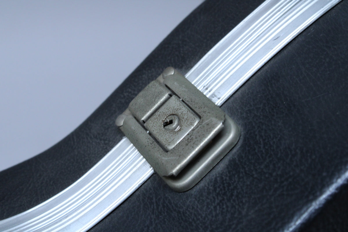 Close-up of the black textured case, showing a tarnished, rectangular metal latch with a keyhole, and silver trim.
