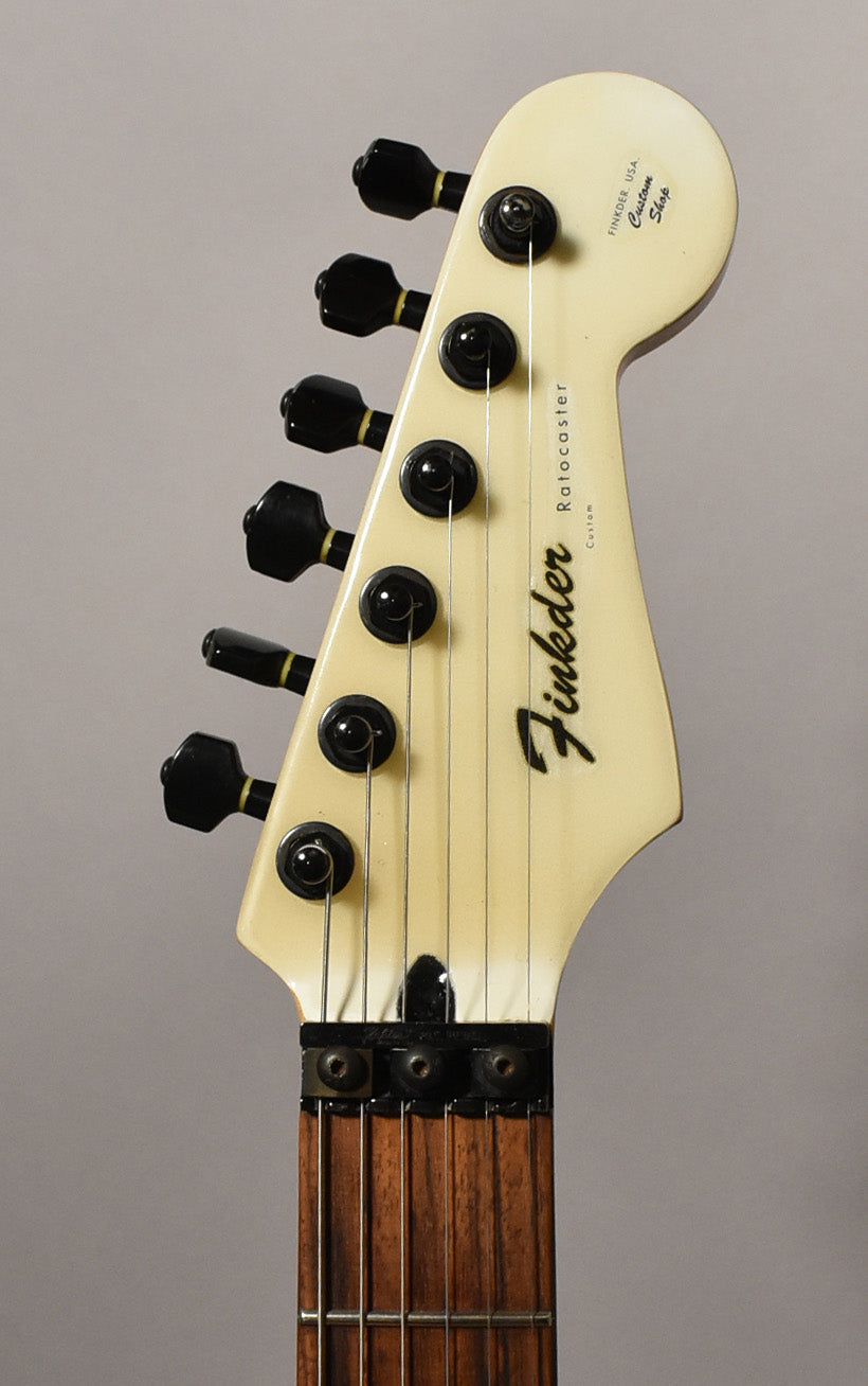 Close-up of the guitar's cream-colored headstock with black tuners, showing a locking nut and dark wood fretboard.