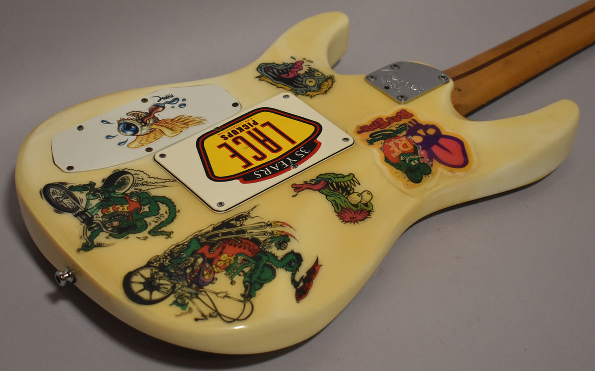The back of the cream guitar body is covered in colorful monster stickers, with a metal neck plate and a light wood neck.