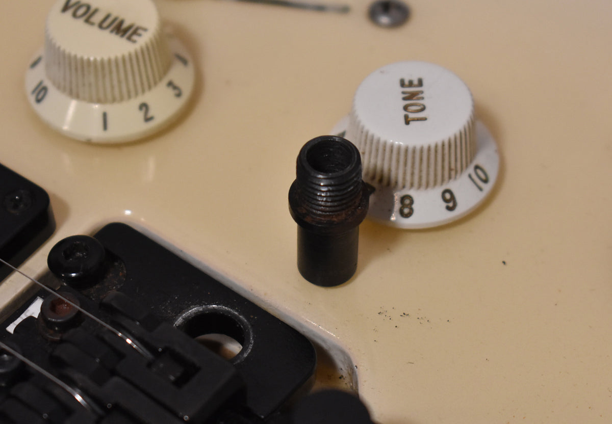 Close-up of the guitar's cream body, showing a black tremolo arm insert, white volume and tone knobs, and light wear.