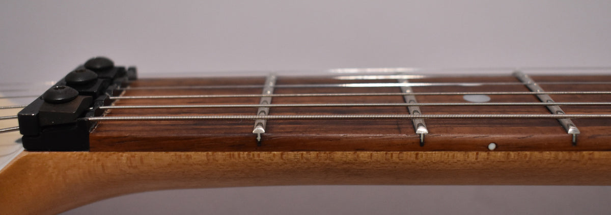 A close-up of the guitar's neck and fretboard from the side, showing a dark wood fretboard, light wood neck, and black locking nut.