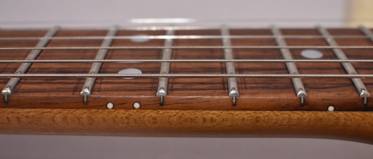 Close-up of the guitar's fretboard, showing dark wood with white dot inlays and side markers, and a lighter wood neck.