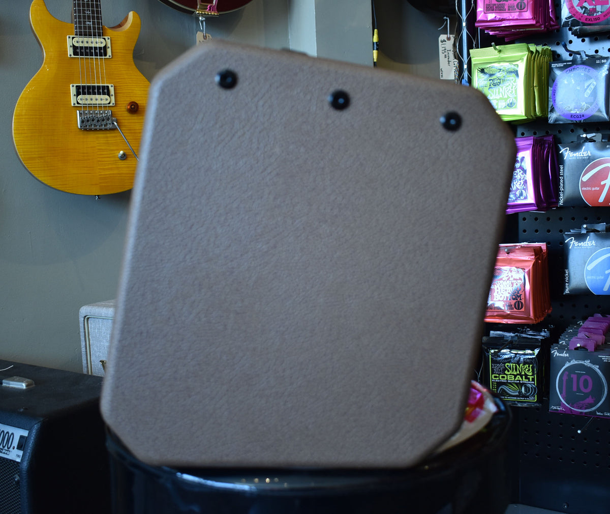 The brown textured amplifier is seen from the back, angled slightly right, with three black feet visible on top.