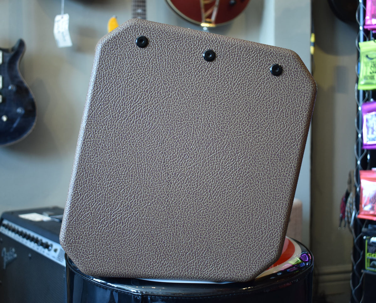 The back of a brown textured guitar amplifier with three black screws, sitting on a black stool in a guitar shop.