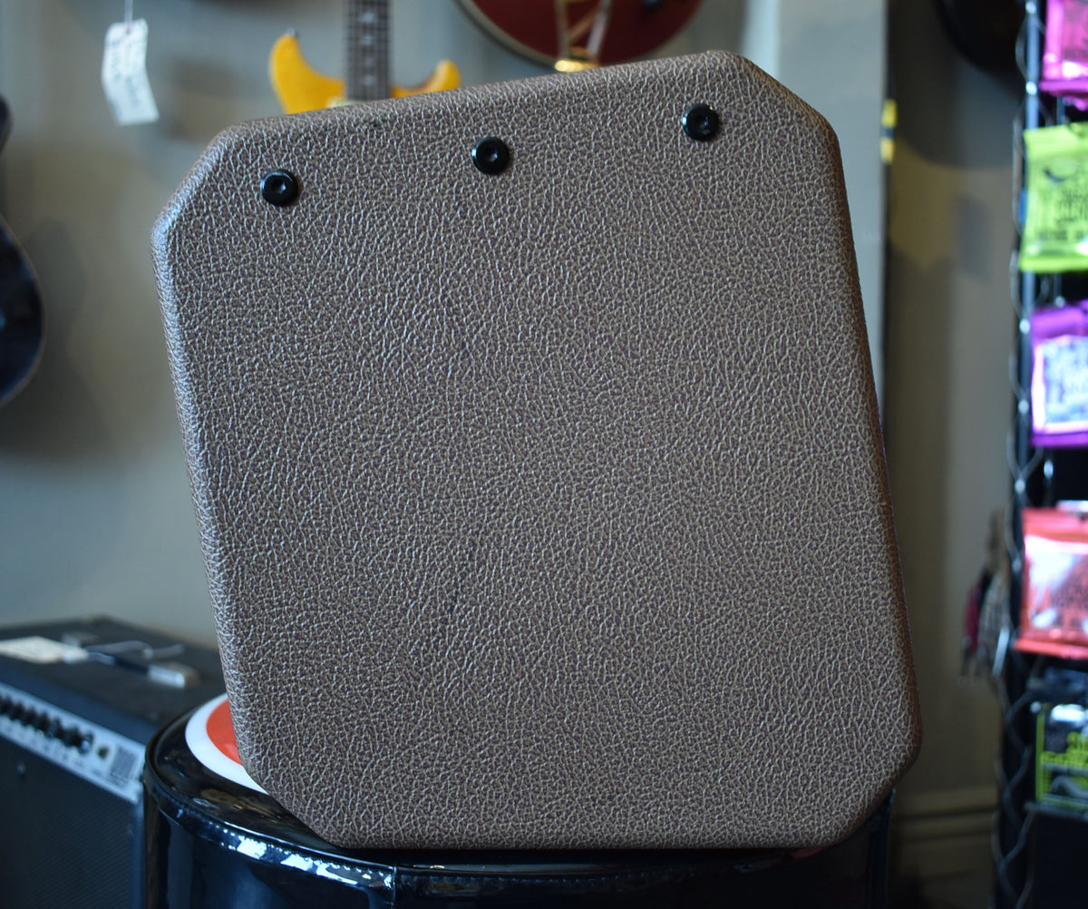 The brown textured tolex amplifier is angled, showing its back panel with three black screws across the top edge.