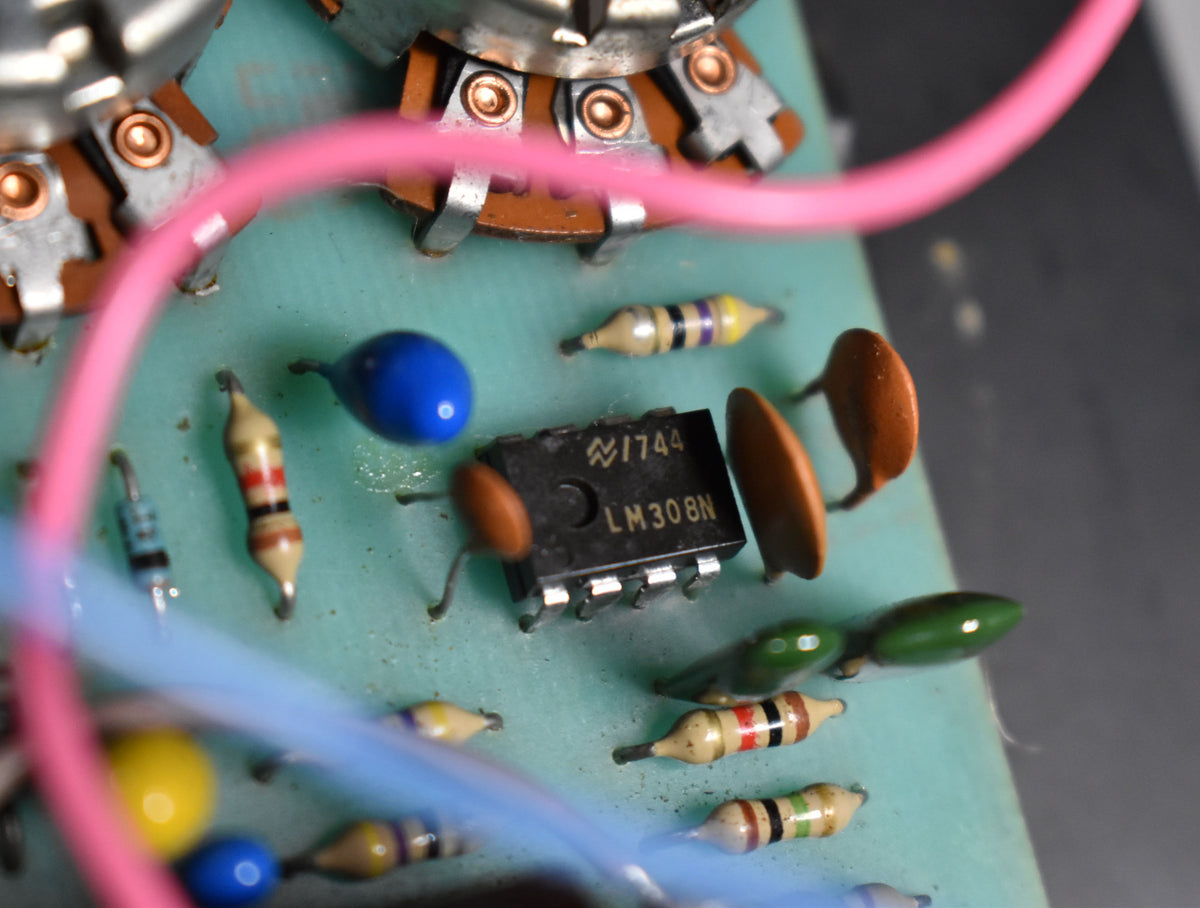 Close-up of the circuit board, showing a black integrated circuit, various colorful resistors and capacitors, and pink and blue wires.