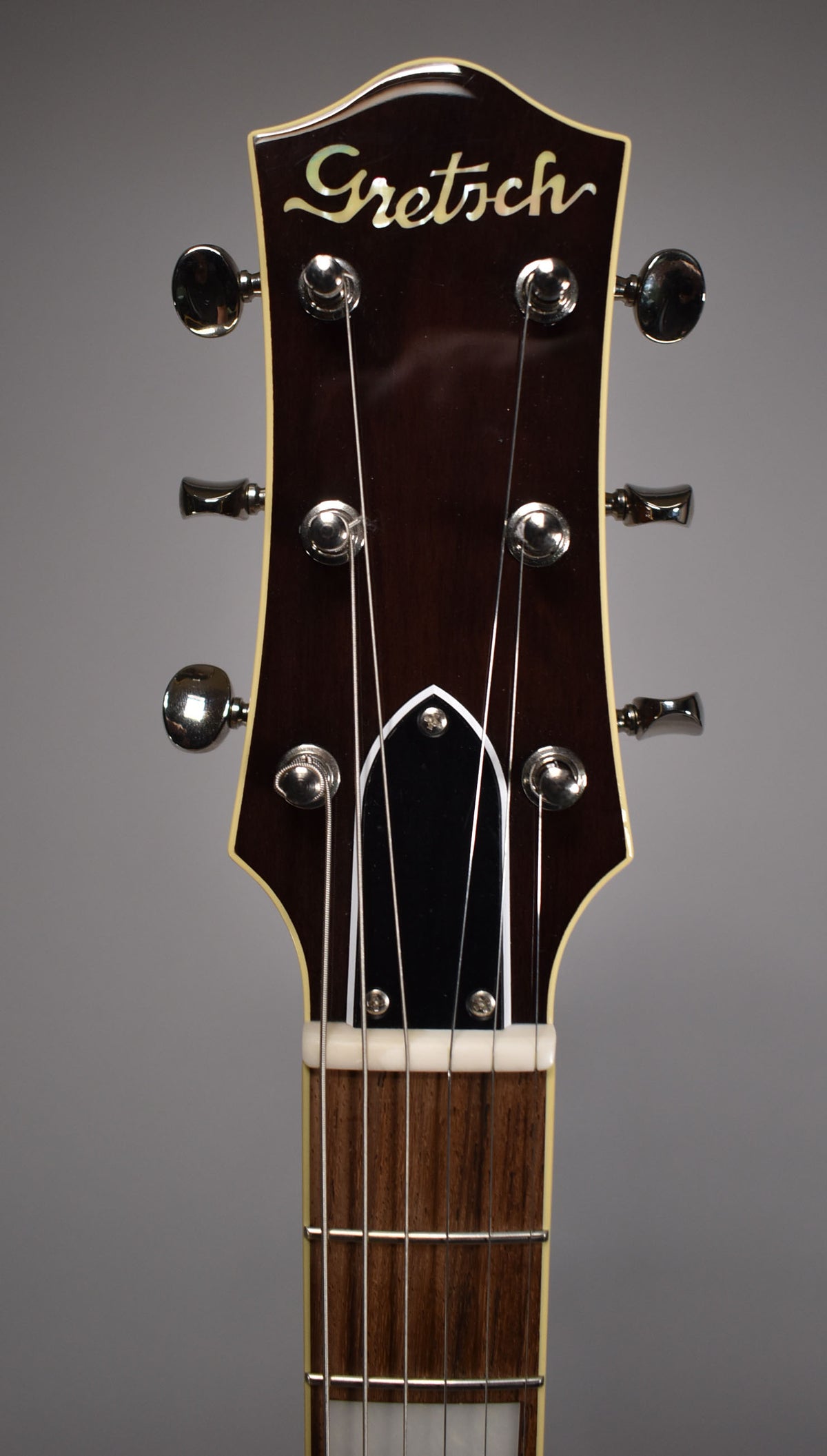 The dark brown headstock with cream binding and mother-of-pearl inlay is framed from the nut up, showing six chrome tuners.