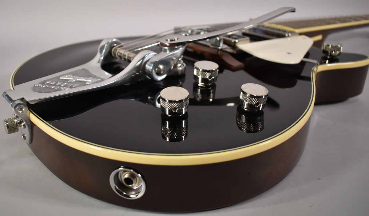 The black guitar body, with cream binding, shows three chrome knurled control knobs and a Bigsby vibrato tailpiece.