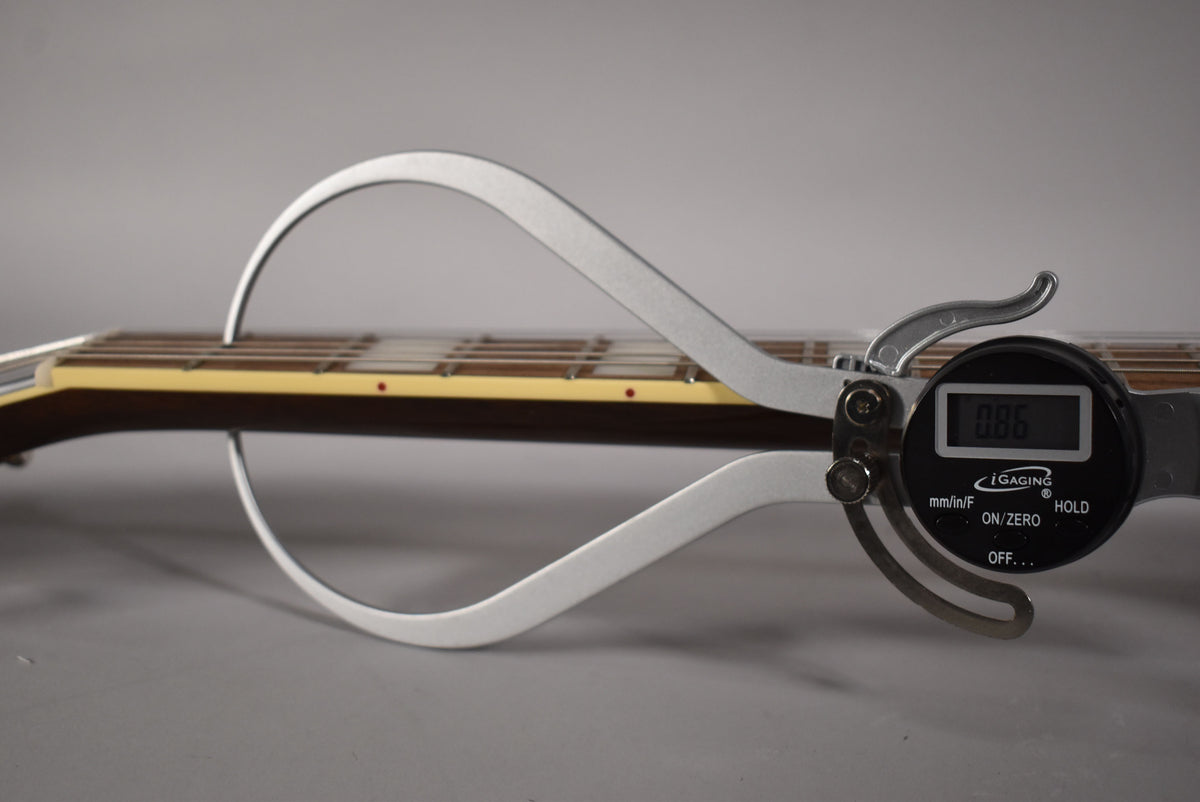 A digital caliper measures the dark brown fretboard with cream binding and red dot markers, displaying "0.86".
