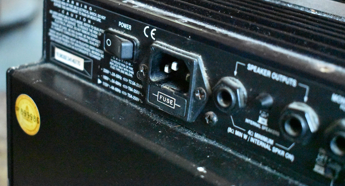 Close-up of the amp's dusty black rear panel, showing the power switch, IEC inlet with fuse, and two speaker output jacks.