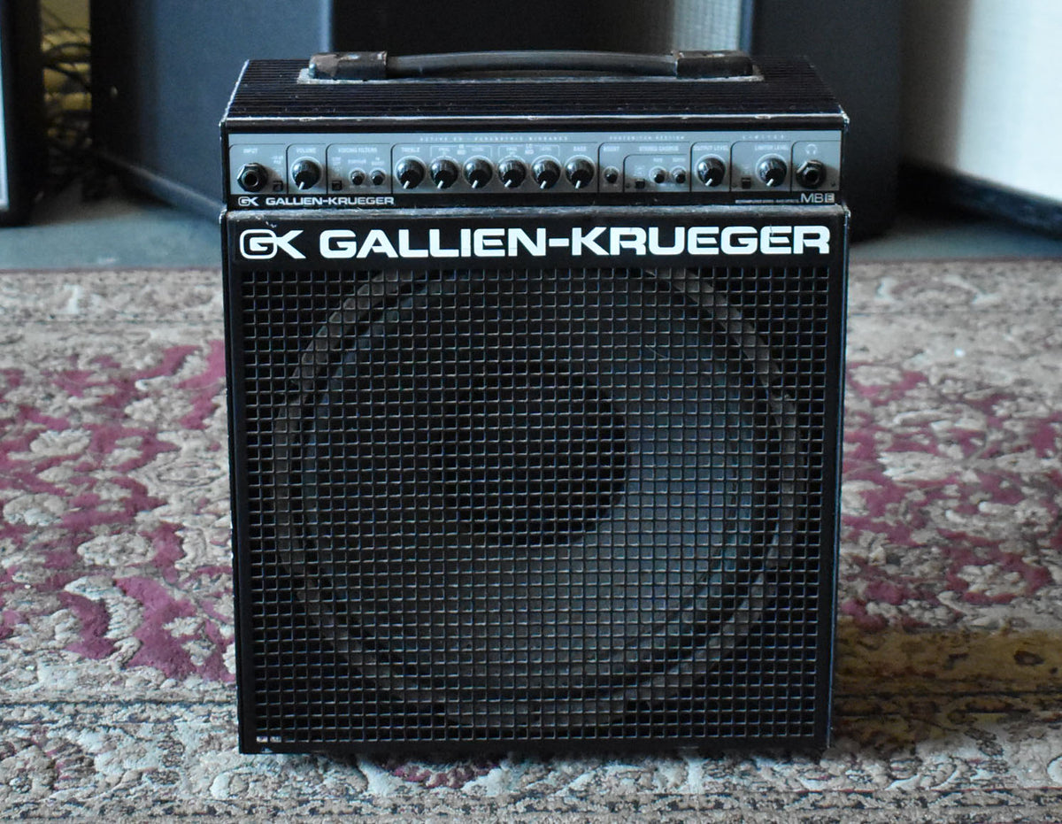 Front view of a black combo amp with a metal grille, a top handle, and a silver control panel with many black knobs.