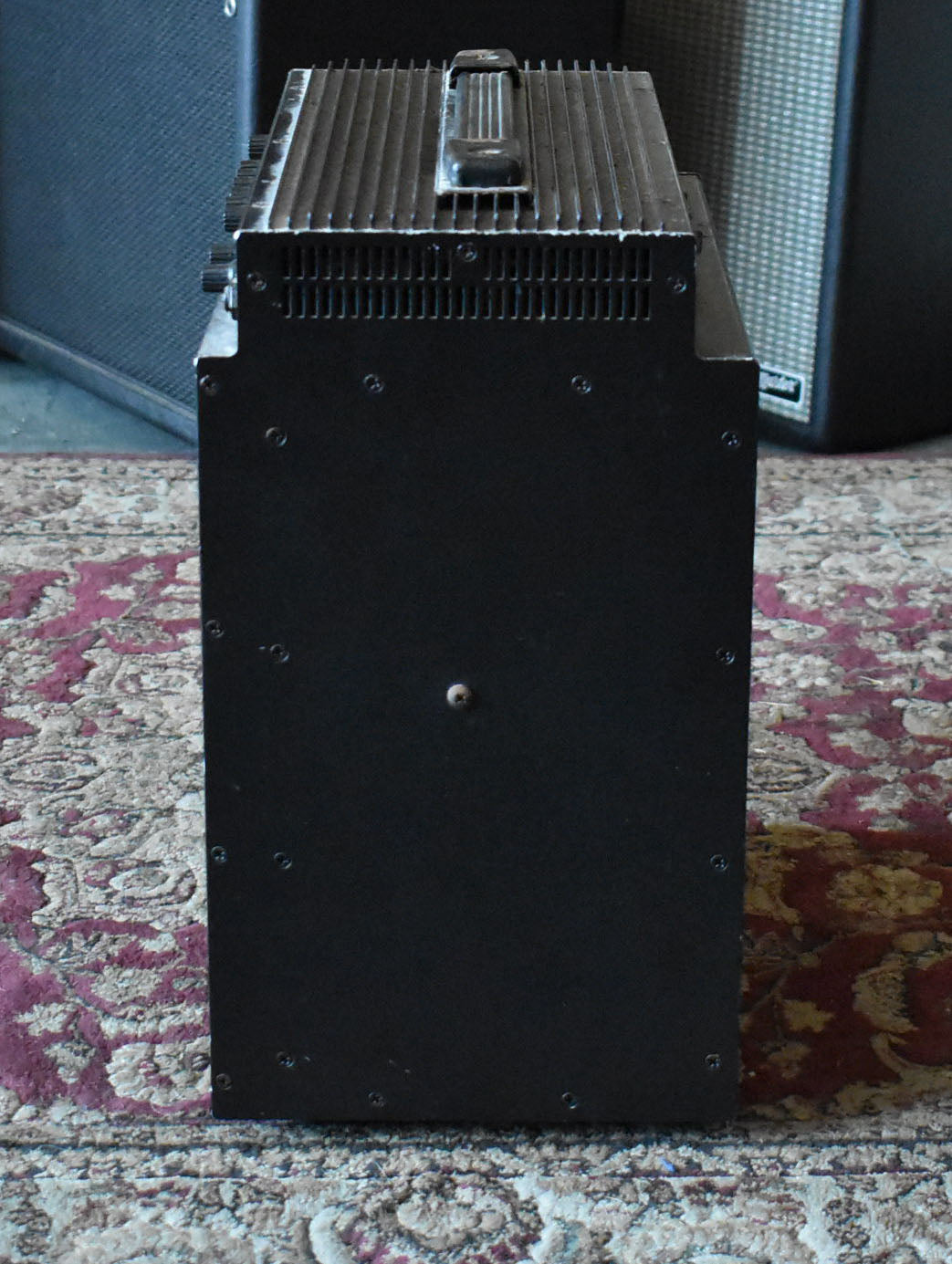 The black combo amp is viewed from the right side, showing a top handle, ribbed heat sink, and a single visible screw on the side.