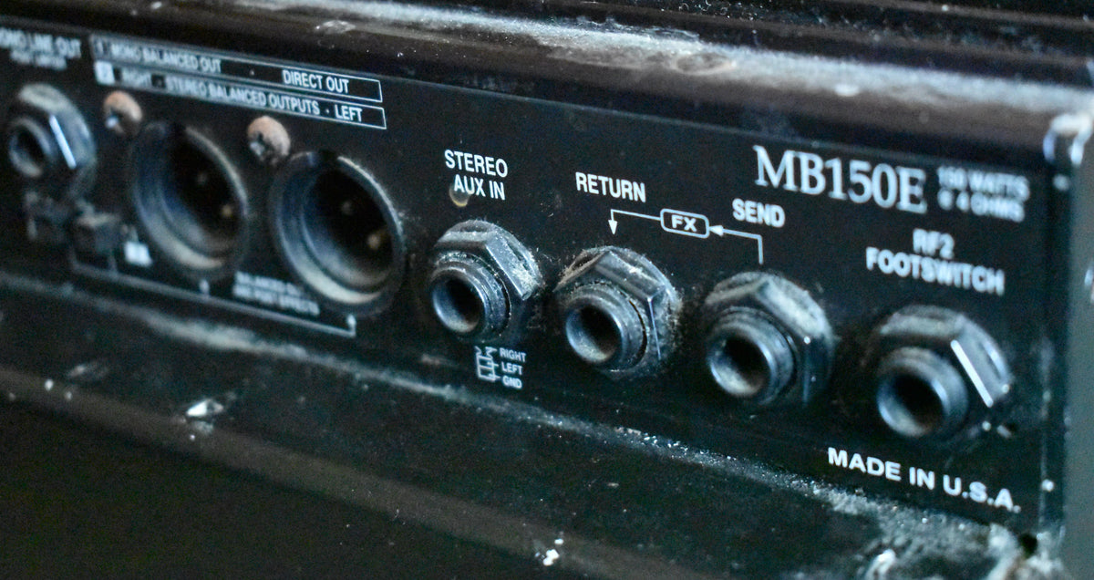 Close-up of the amplifier's dusty black rear panel, showing various input/output jacks and XLR ports, with some scuffs and wear.
