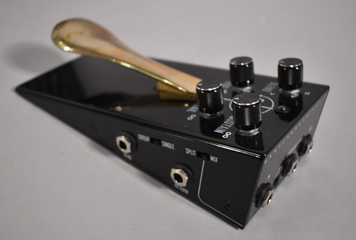 A black gloss pedal with a brass-colored sustain bar, four black knurled knobs, and multiple input/output jacks on the sides.
