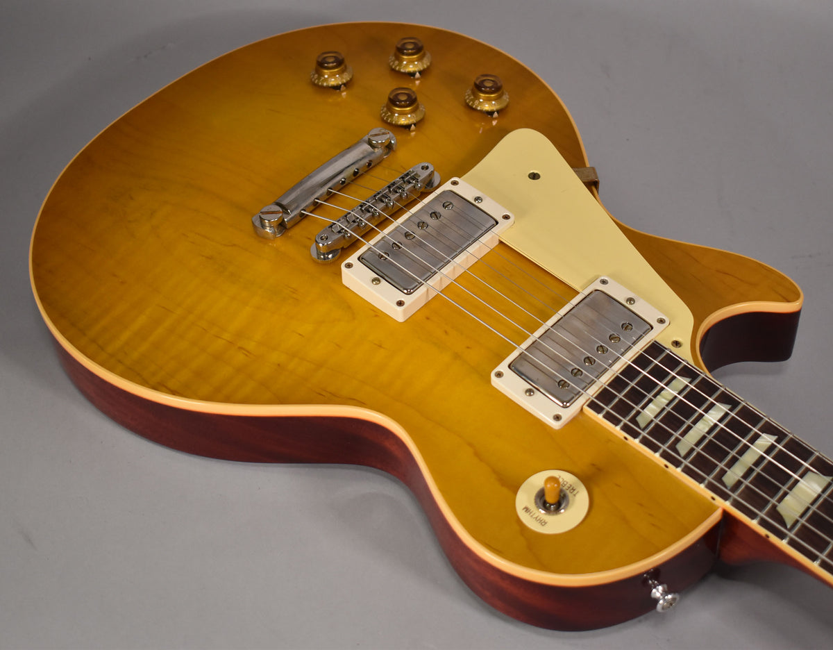 Close-up of a left-handed lemon burst electric guitar, showing the flamed maple top, cream pickguard, and two humbucker pickups.