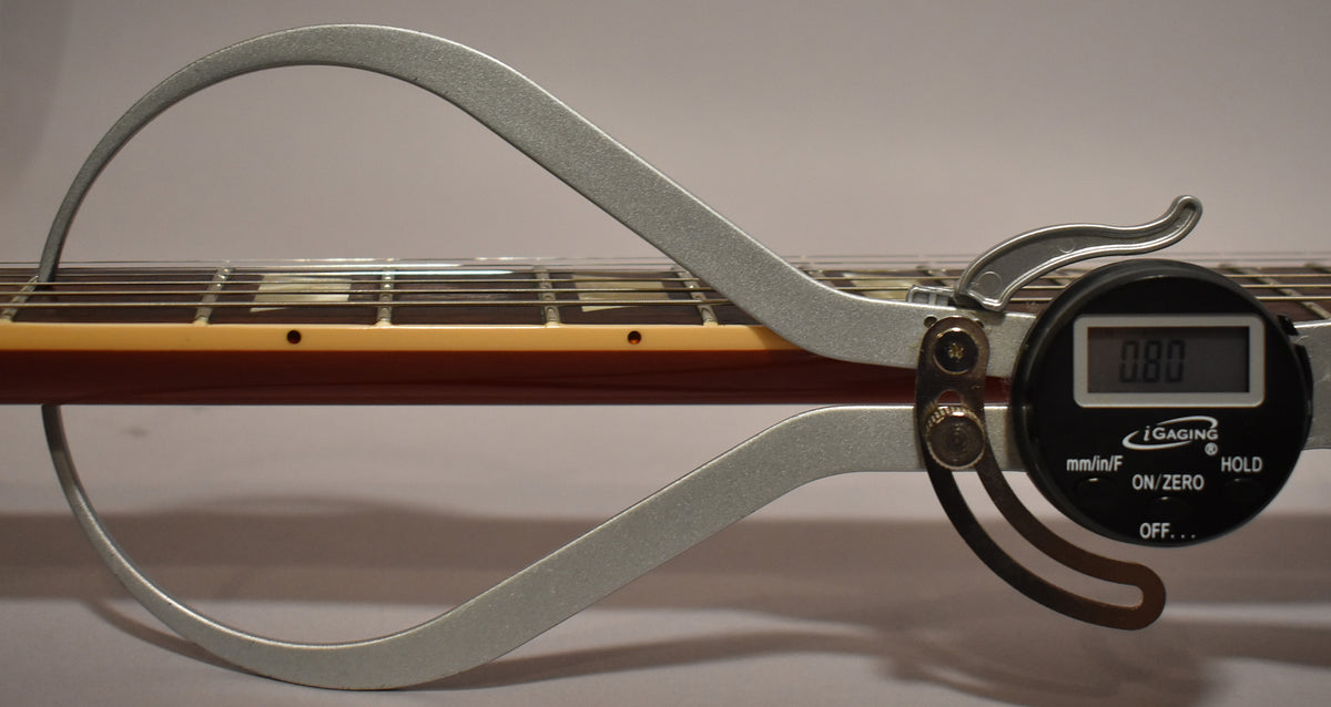 A digital caliper measures the neck thickness at the 1st fret, showing 0.80 inches, with trapezoid inlays visible.