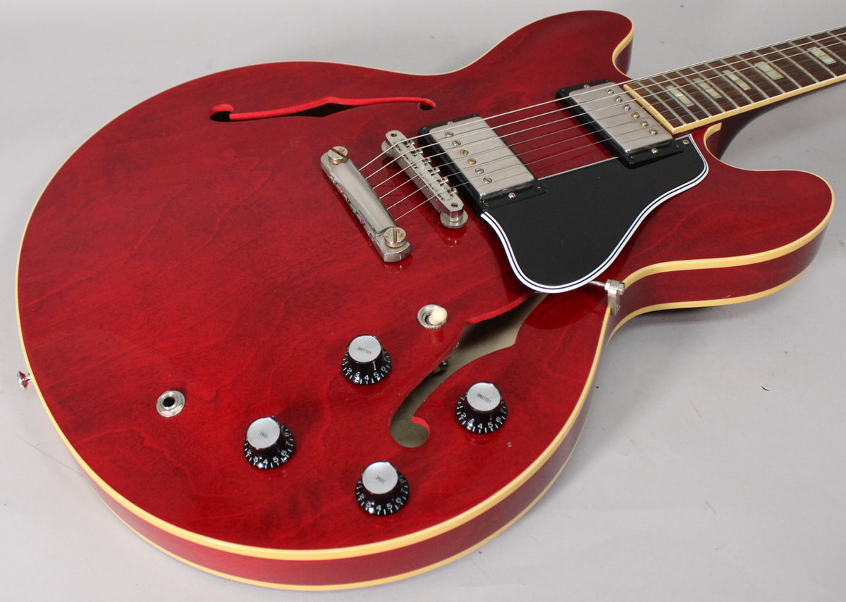 Cherry red semi-hollowbody guitar, angled from above, showing the body, f-holes, pickups, pickguard, bridge, and four control knobs.