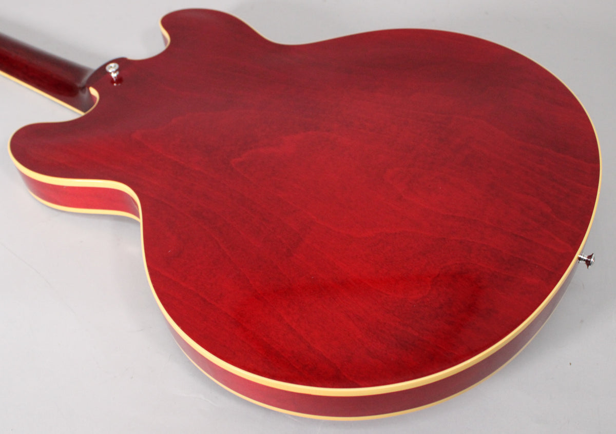 The back of the cherry red semi-hollow guitar, showing its grain and light aging, with cream binding and two strap buttons.