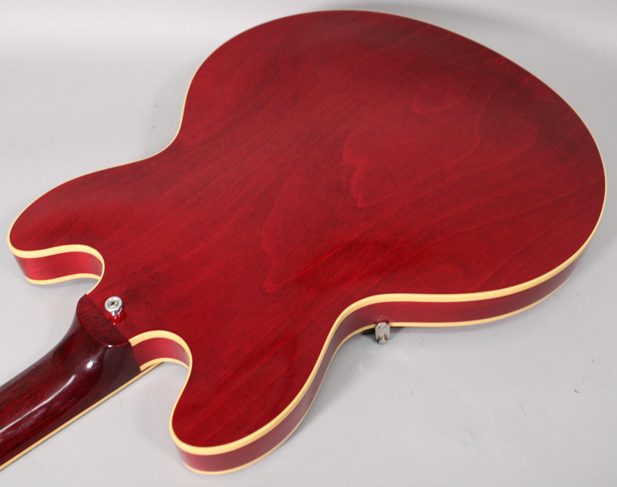 The back of the cherry red hollow-body guitar, showing the neck joint, body binding, and subtle wood grain through the finish.