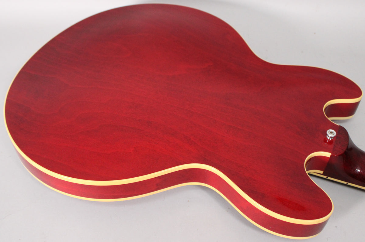 The back of a cherry red ES-335 guitar, showing the body's grain, cream binding, and the strap button near the neck joint.