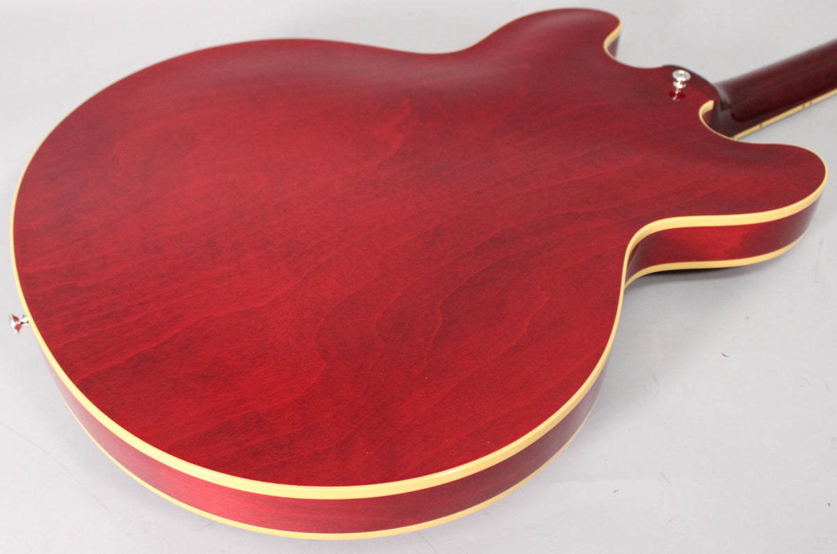 The back of the cherry red hollow body guitar shows wood grain, light aging, and cream binding along the edges.