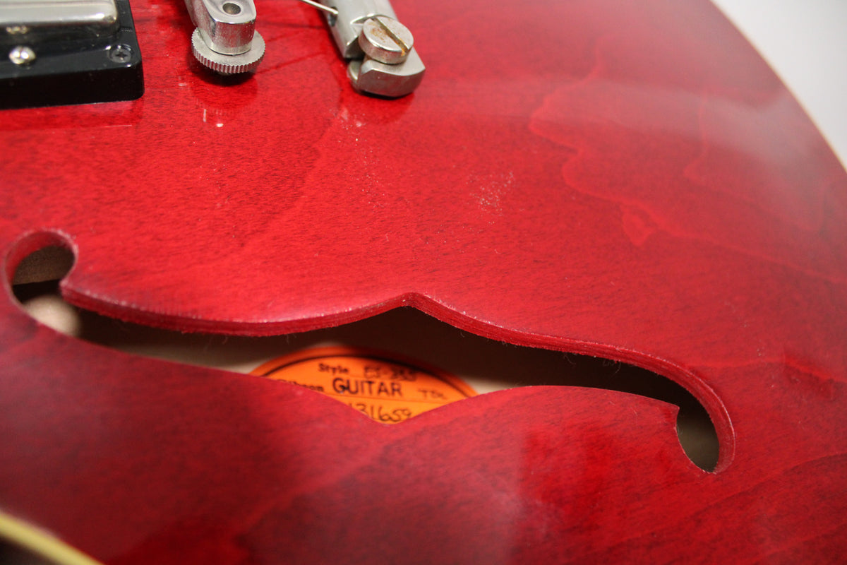 Close-up of the cherry red body, showing the f-hole with a visible orange label inside, and light finish wear near the bridge.