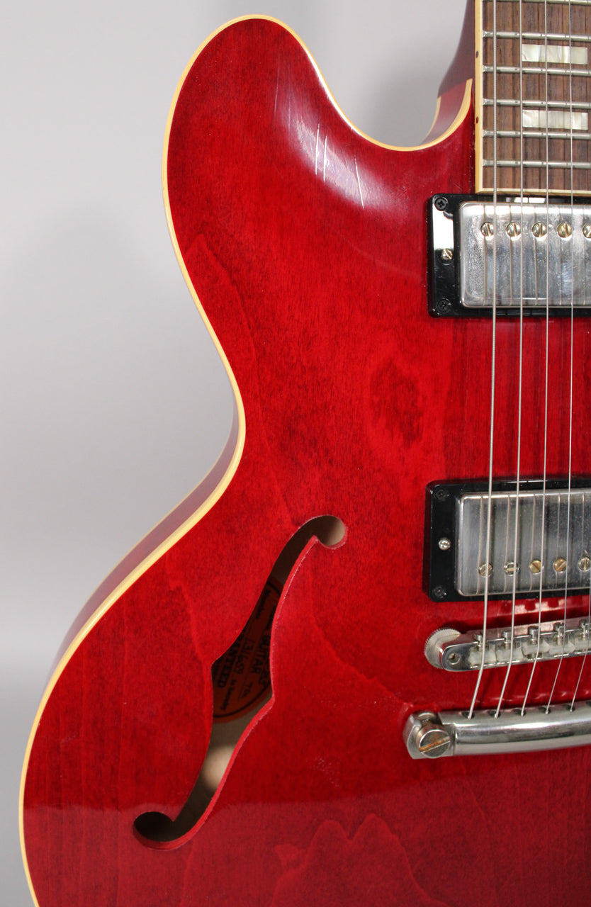 Close-up of the cherry red body, showing the upper bout with finish wear, f-hole, two humbuckers, and bridge.