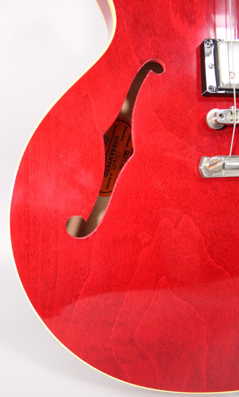 Close-up of the cherry red body, showing the f-hole with a visible label inside, binding, and a chrome bridge pickup.