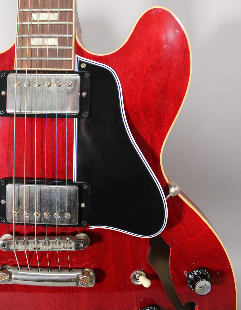 Close-up of the cherry red body, showing the black pickguard, two humbuckers, bridge, and volume knob with light aging.