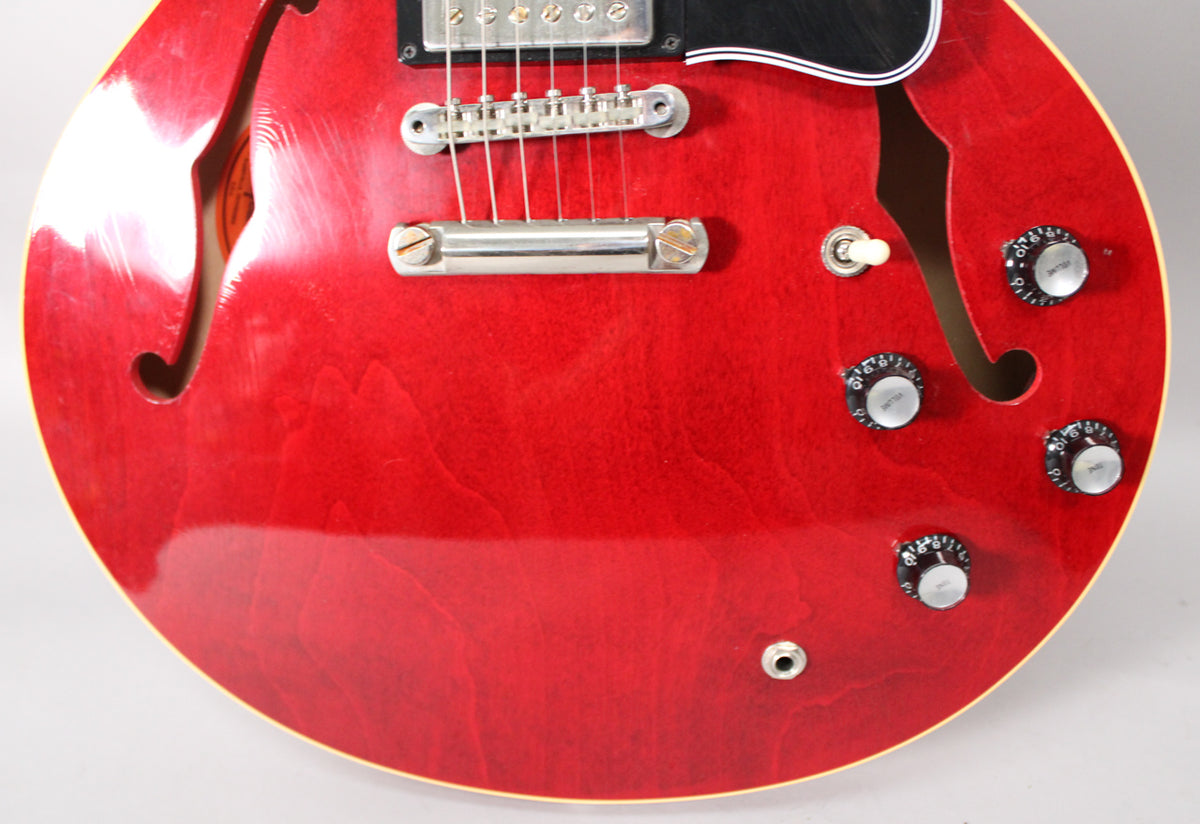 The lower bout of a cherry red semi-hollow guitar, showing the bridge, tailpiece, pickup selector, four control knobs, and output jack.