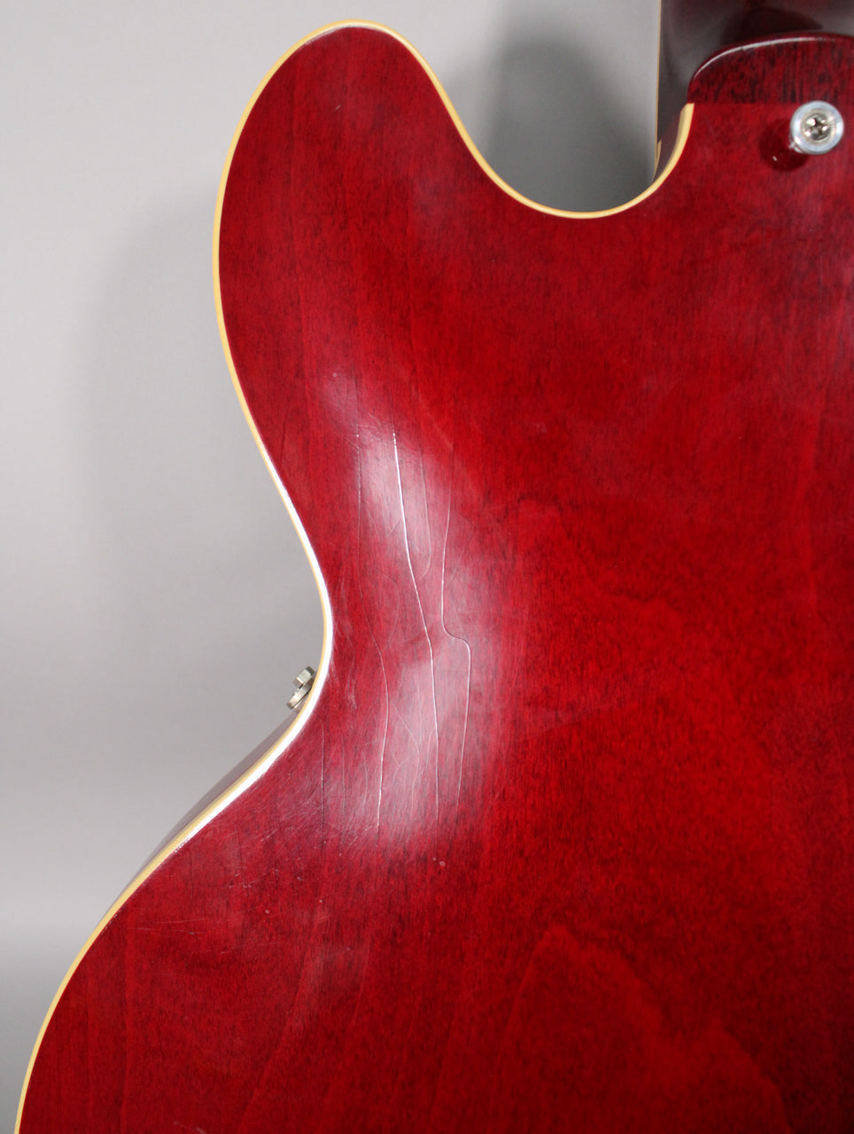 Close-up of the cherry red guitar's lower bout and waist from the back, showing extensive finish checking and a strap button.