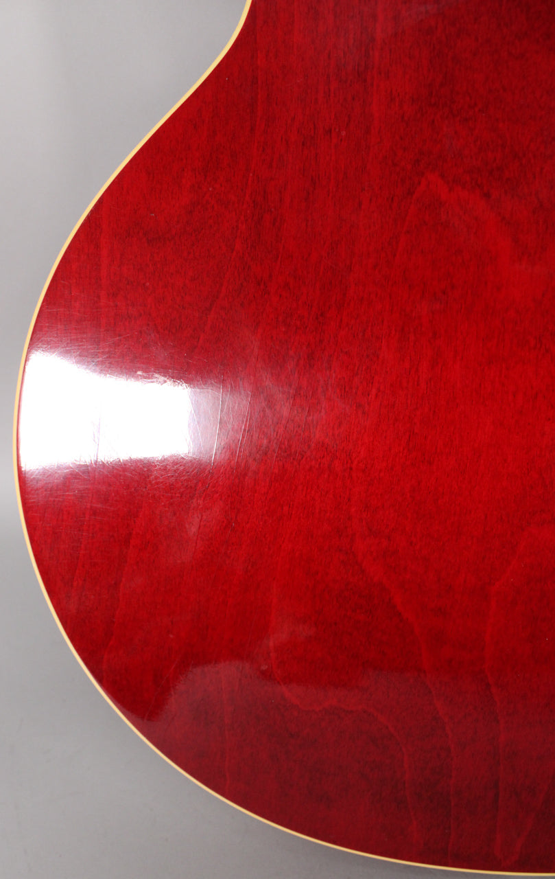Close-up of the guitar's cherry red body, showing light finish checking and wear, with cream binding along the curved edge.