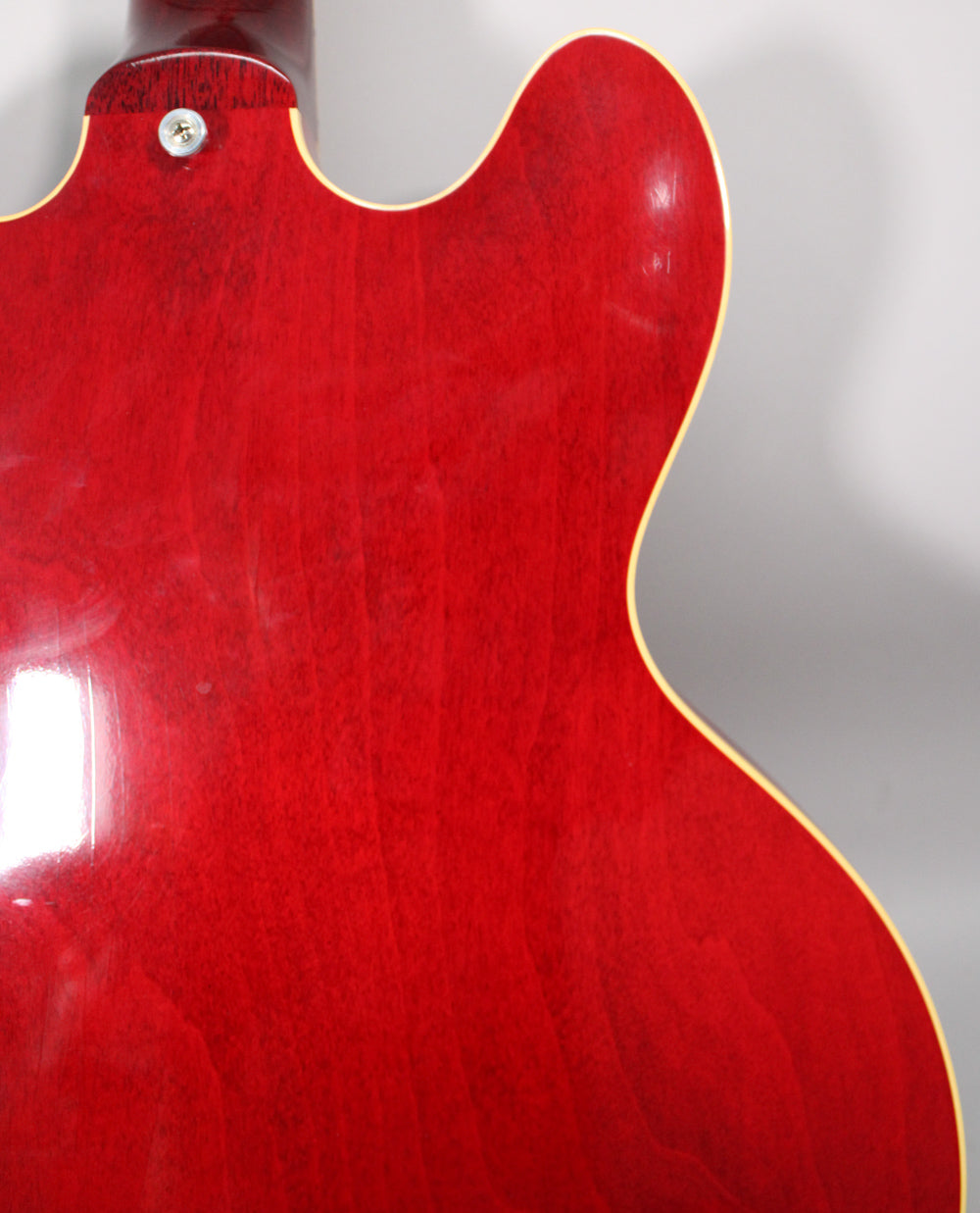 The upper back of a cherry red semi-hollow guitar, showing the neck joint and upper bout with light finish checking.
