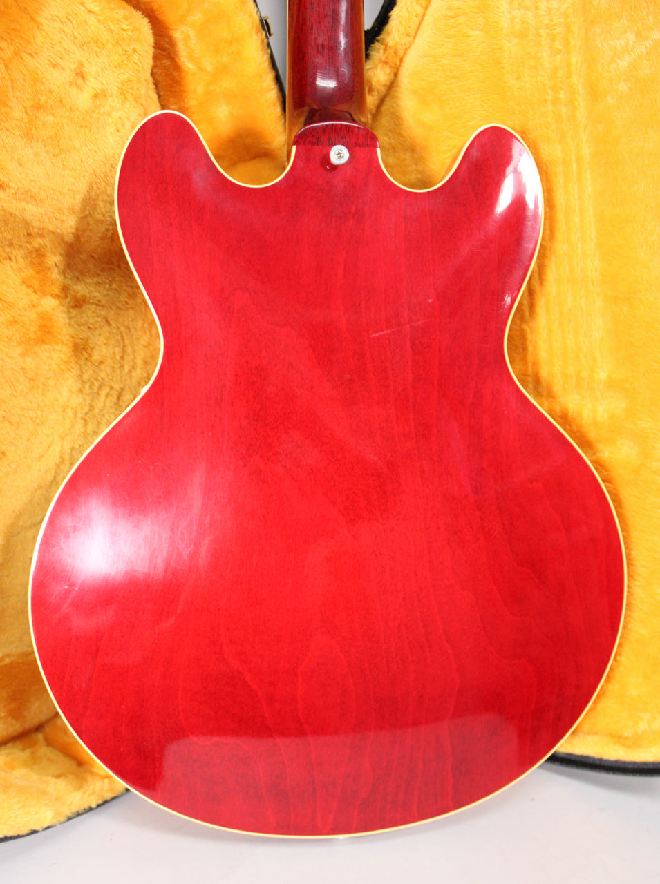 The back of a cherry red hollow-body guitar with a visible wood grain, light finish wear, and a neck joint screw.