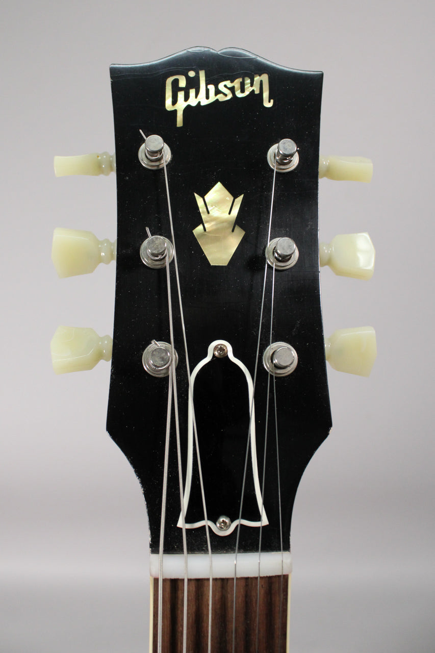 Close-up of the black headstock with a mother-of-pearl crown inlay, six cream tuning pegs, and light finish checking.